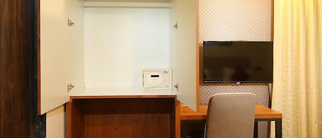 Habitación compacta con escritorio de madera, una silla, televisor y un pequeño dispositivo blanco sobre el escritorio.