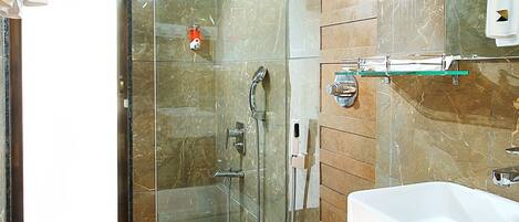 Un baño moderno con ducha de vidrio, lavamanos blanco y pared de azulejos de mármol.