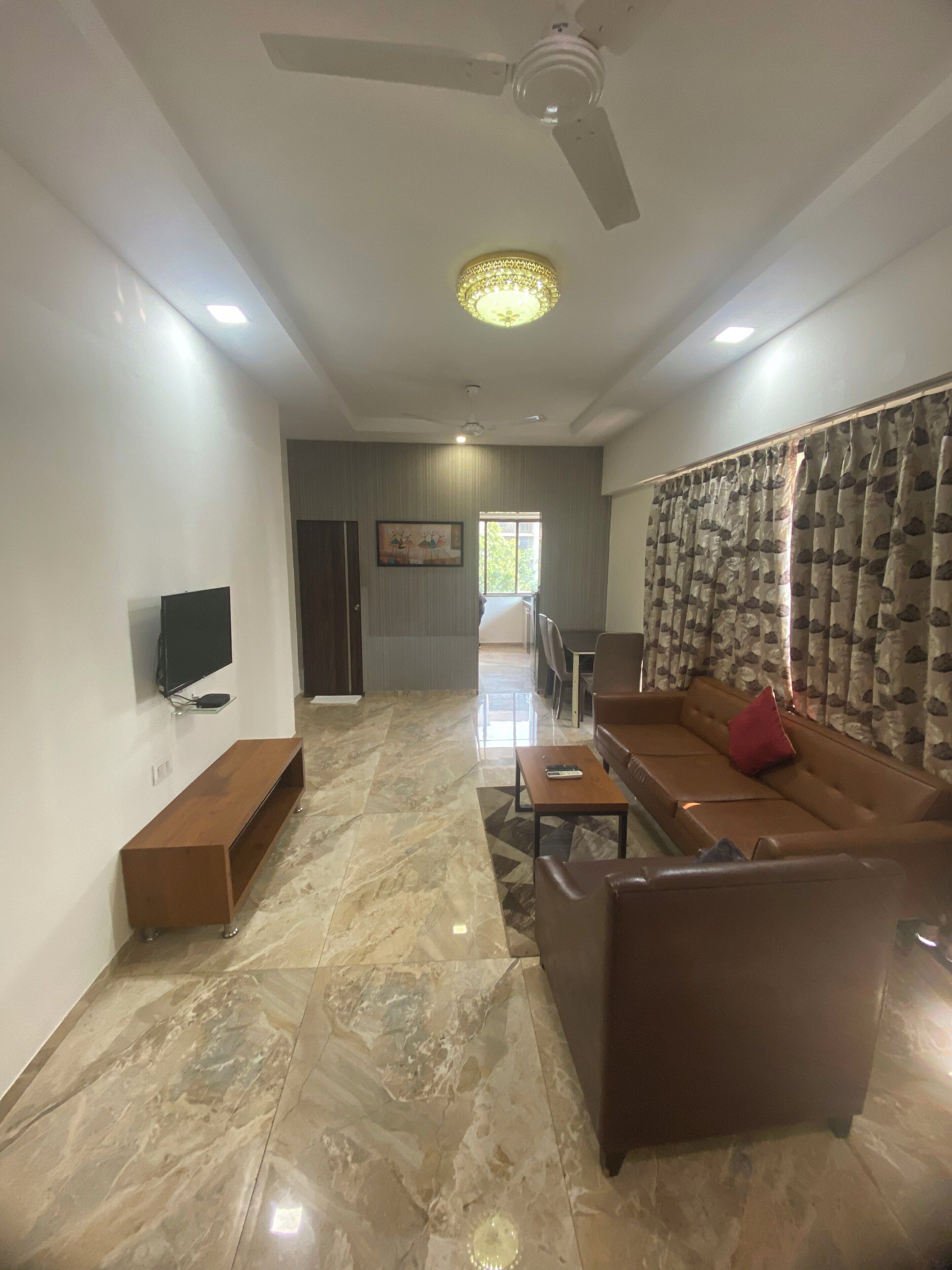 Un vaste salon doté d’un sol en marbre, d’un ventilateur de plafond, d’un téléviseur à écran plat, d’un canapé et d’un coin repas à l’arrière-plan.