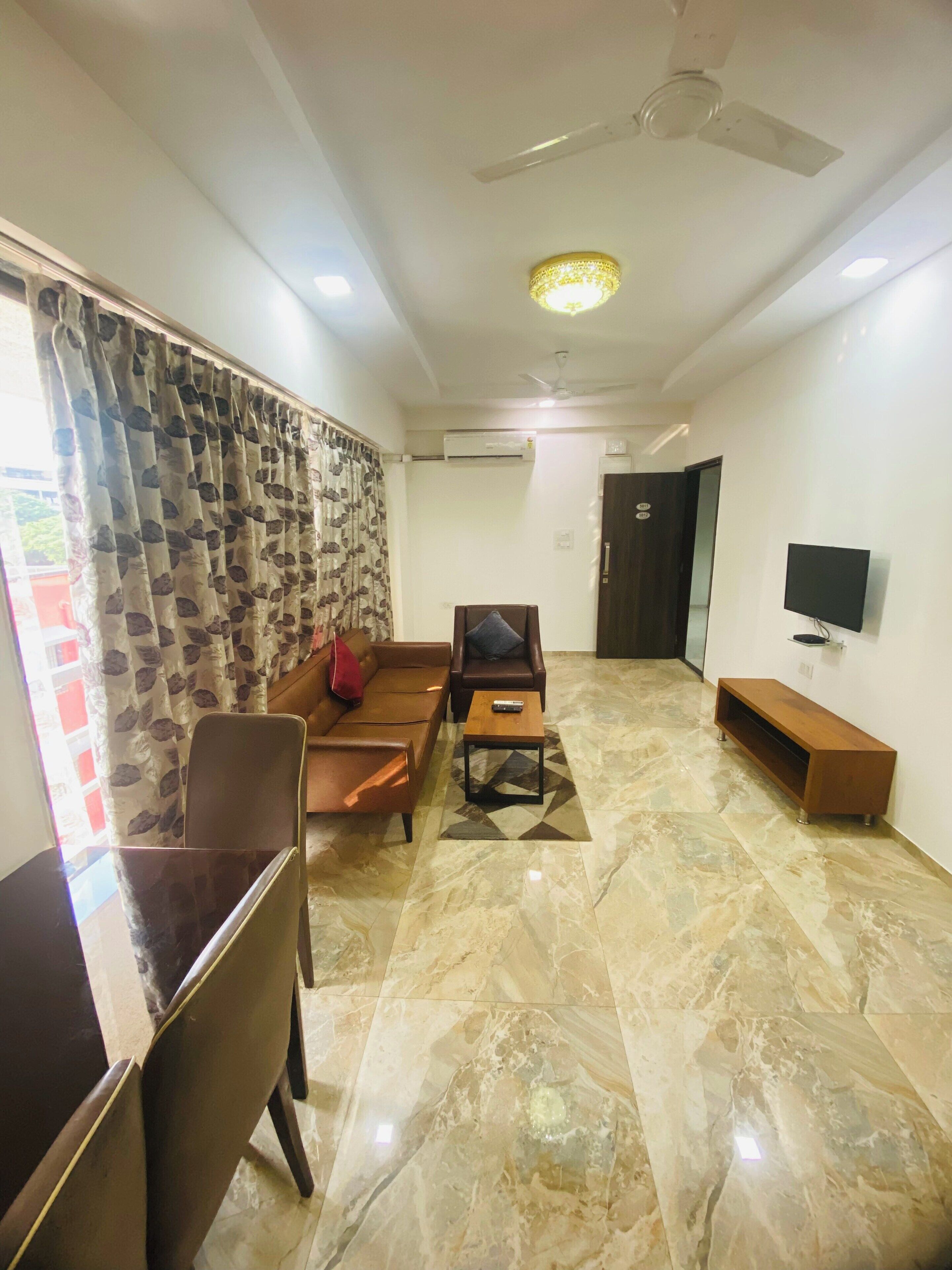 Uma sala de estar com sofá, mesa de centro, televisão e ventilador de teto.
