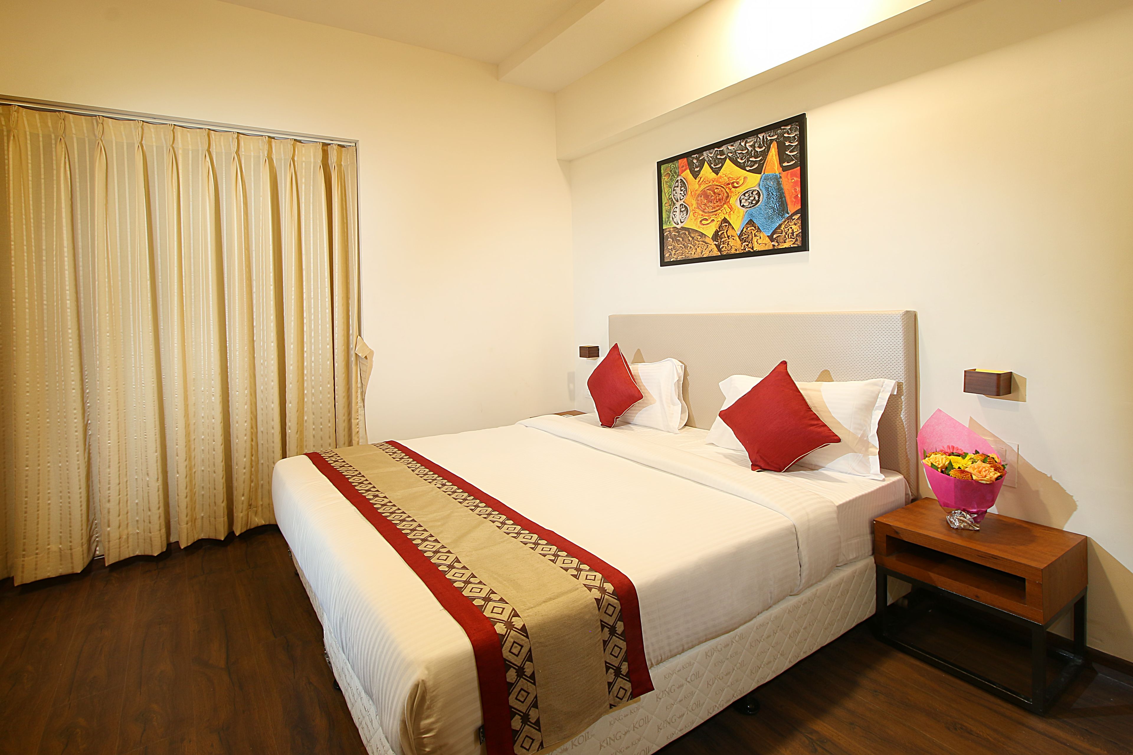 A hotel room with a large bed, a nightstand with a vase of flowers, and a painting on the wall.