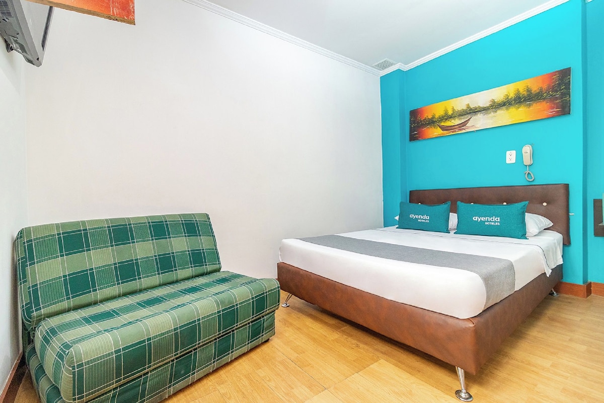 Ein Zimmer mit einem Bett, einem grün karierten Sofa, einem Gemälde an der Wand und einem Telefon auf dem Nachttisch.