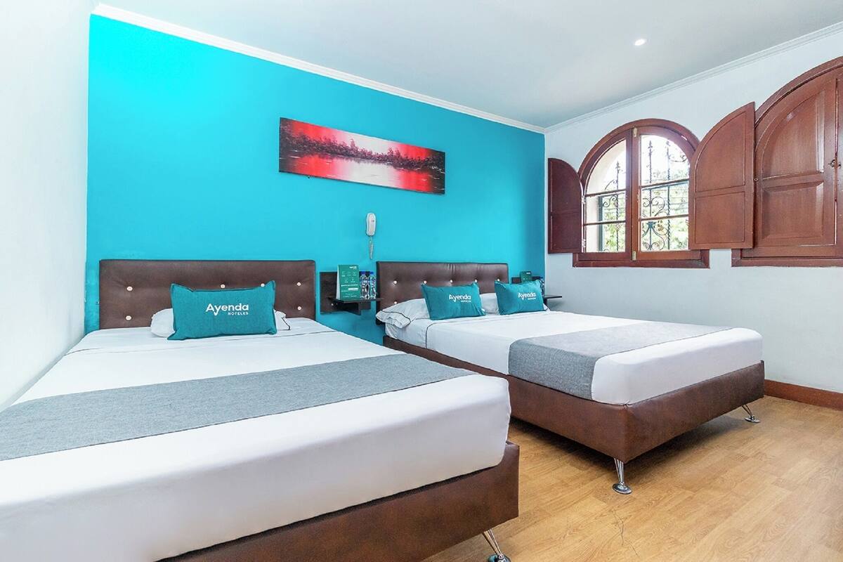 Une chambre d’hôtel avec deux lits, un mur d’accent de couleur turquoise, un tableau, un téléphone sur la table de chevet et des armoires en bois.