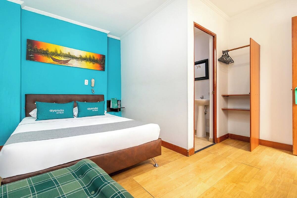 Une chambre d’hôtel avec un lit, un tableau au mur, un téléphone et une porte donnant sur une salle de bain.