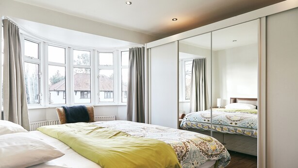 A bedroom with a large window, a mirror, and a bed with a patterned bedspread. - 16 Austin Avenue (Bromley)