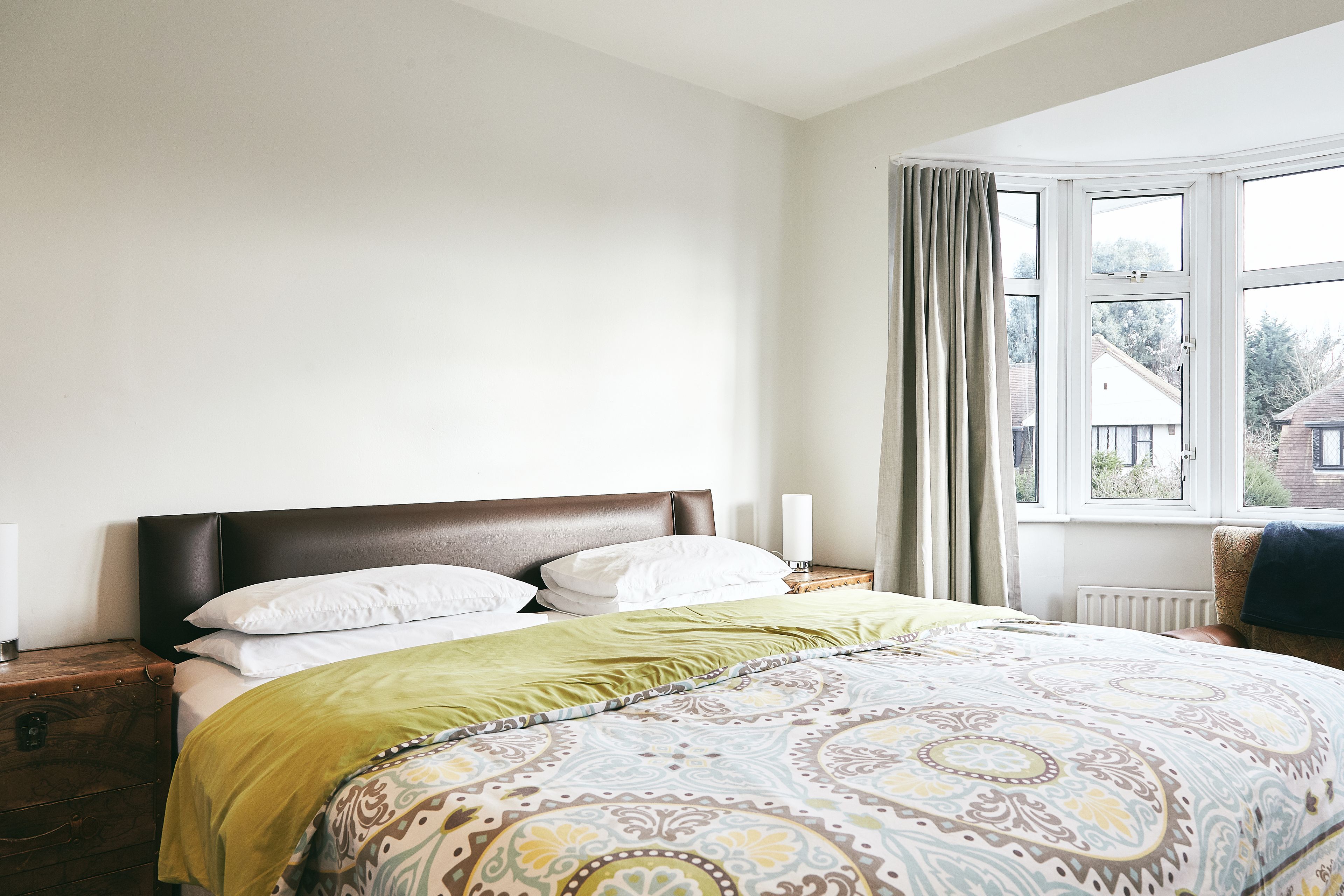 A bedroom with a large bed, a nightstand, a dresser, and a window with curtains.