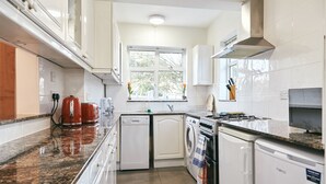 A compact kitchen with white cabinets, a granite countertop, a window, and a built-in oven. - 16 Austin Avenue (Bromley)