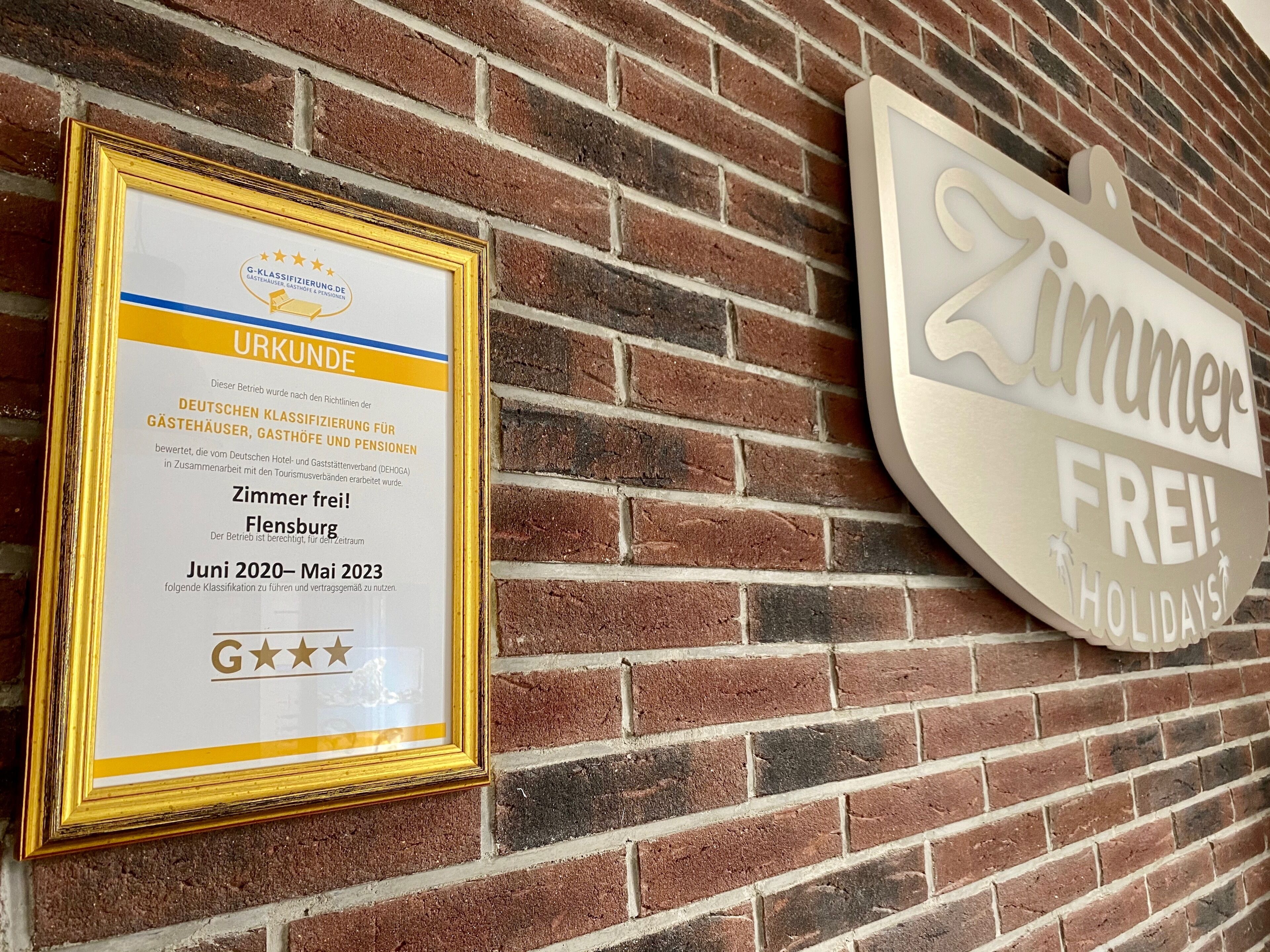 A framed certificate on a brick wall and a sign that reads "Zimmer frei" (Rooms available).