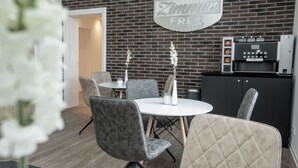 A modern dining area with grey upholstered chairs, a white round table, and a sign that reads "Zimmer FREI".
