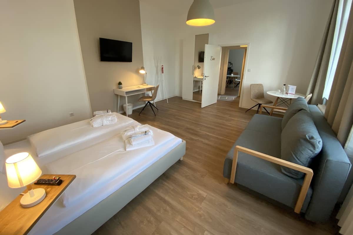 A hotel room with a bed, a desk, a chair, a sofa, and a TV.