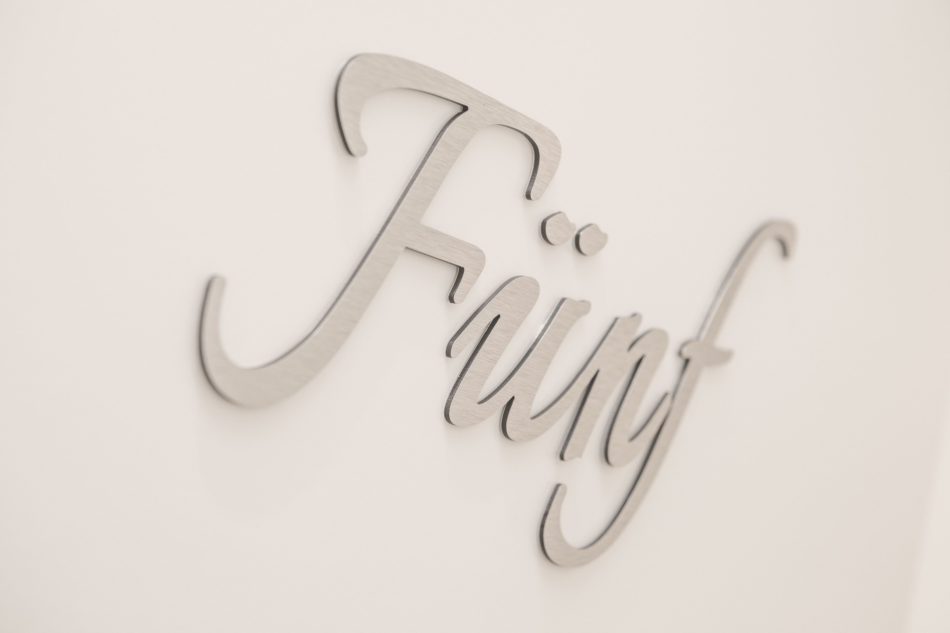 Une enseigne fixée au mur, sur laquelle est inscrit le mot « Fünf » en caractères cursifs.