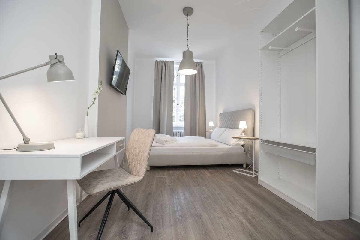 A modern hotel room with a desk, chair, bed, bedside tables, and a TV.
