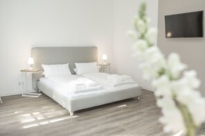 A modern bedroom with a bed, two bedside tables, a flat-screen TV, and a wooden floor. - Zimmer FREI Boardinghouse (Flensburg)