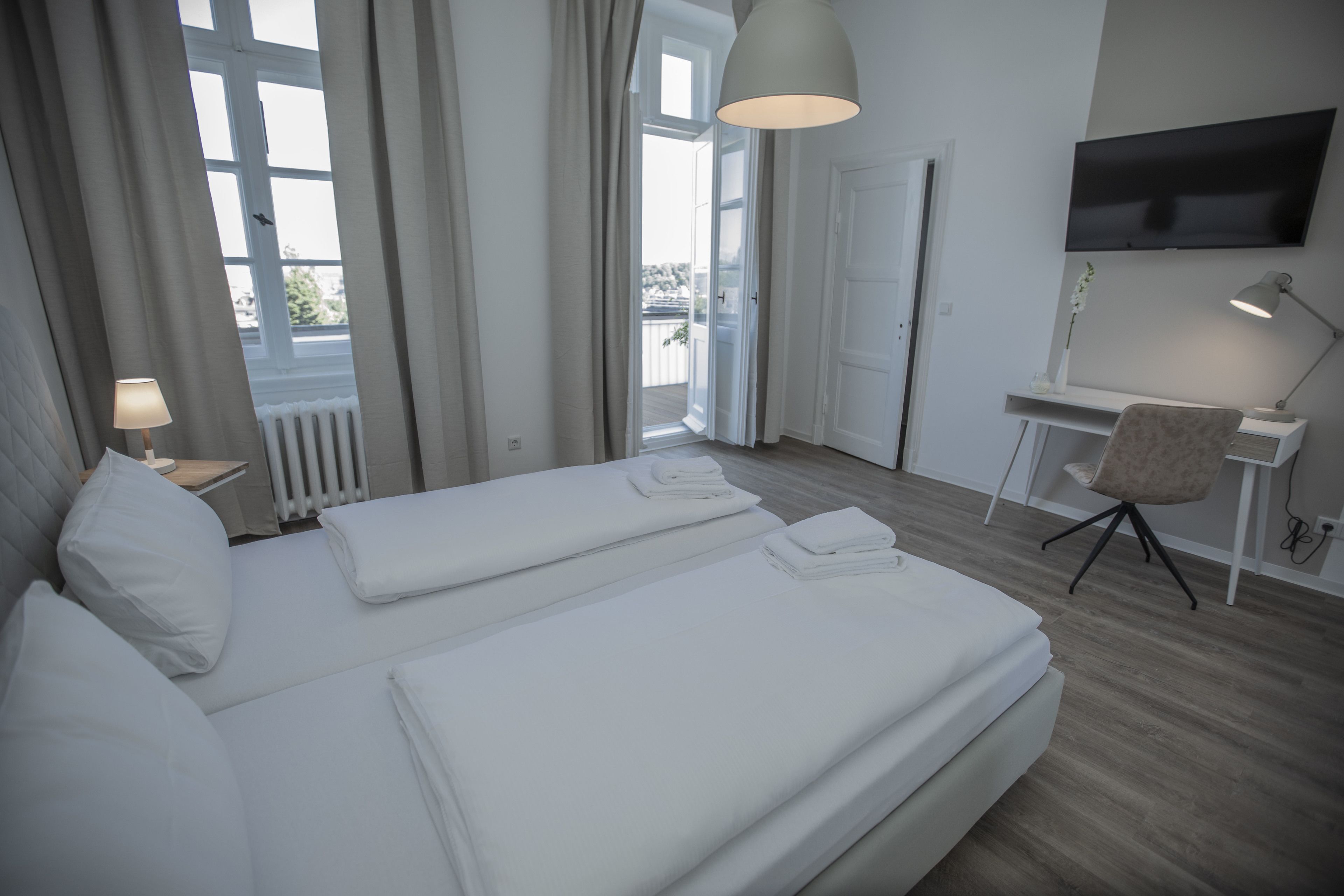 A hotel room with two beds, a desk, a chair, a TV, and a view of the outdoors.