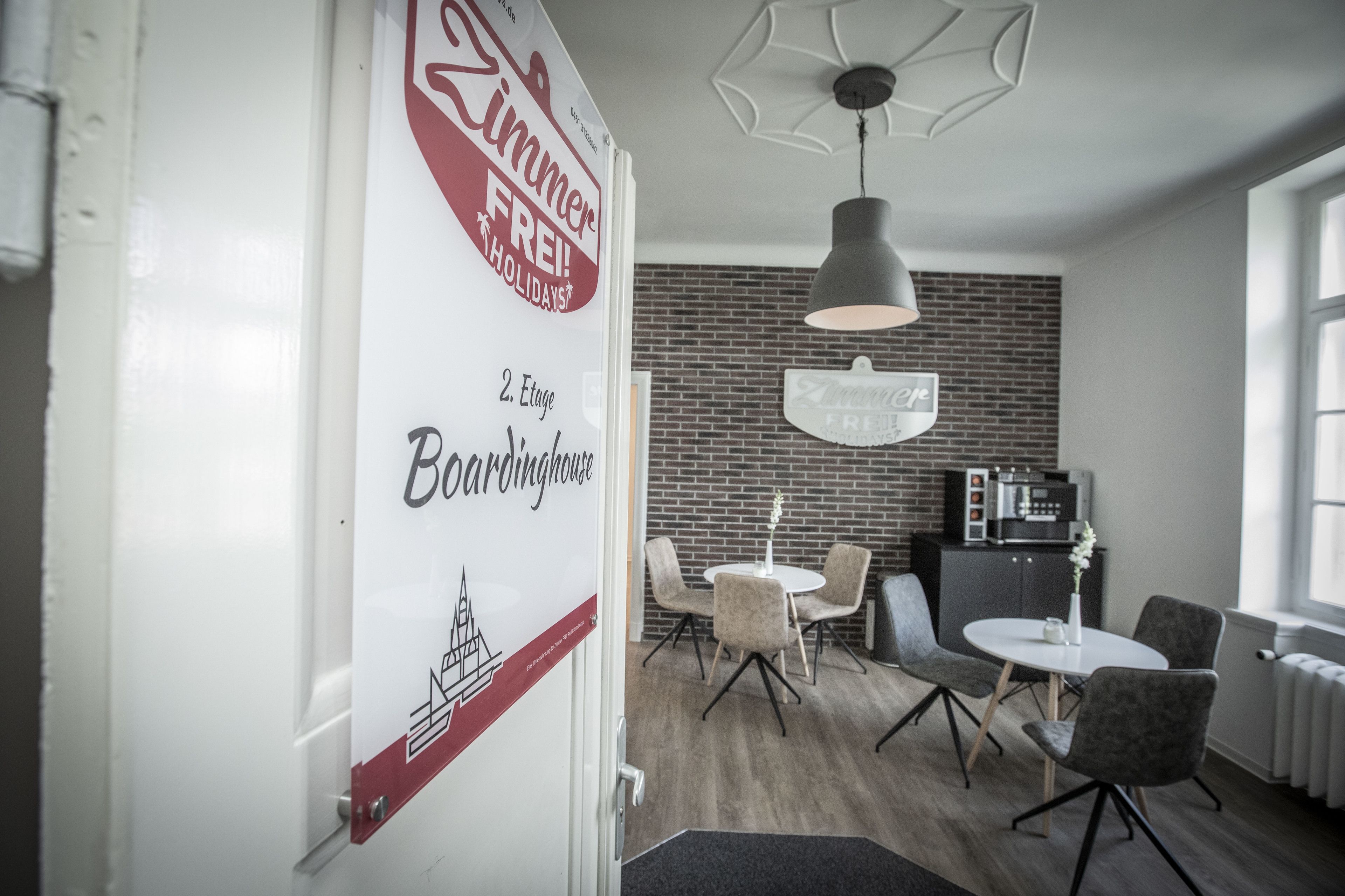 A modern interior with a dining area featuring round tables and chairs, a kitchen area with a microwave and cabinets, and a brick wall.