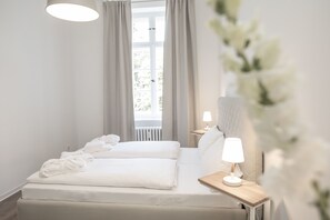 Una habitación de hotel moderna con una cama grande, una mesita de noche con lámpara y una ventana con cortinas.