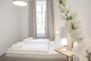 A modern hotel room with a large bed, a bedside table with a lamp, and a window with curtains.