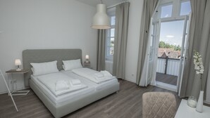 A modern bedroom with a large bed, bedside tables, a chair, and a view of the outdoors through a large window.
