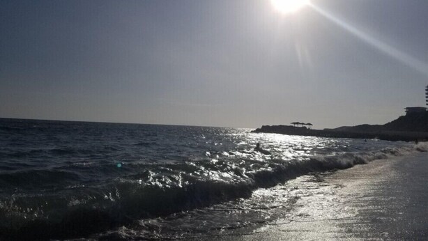 Een strand met golven, een heldere lucht en de zon die schijnt.