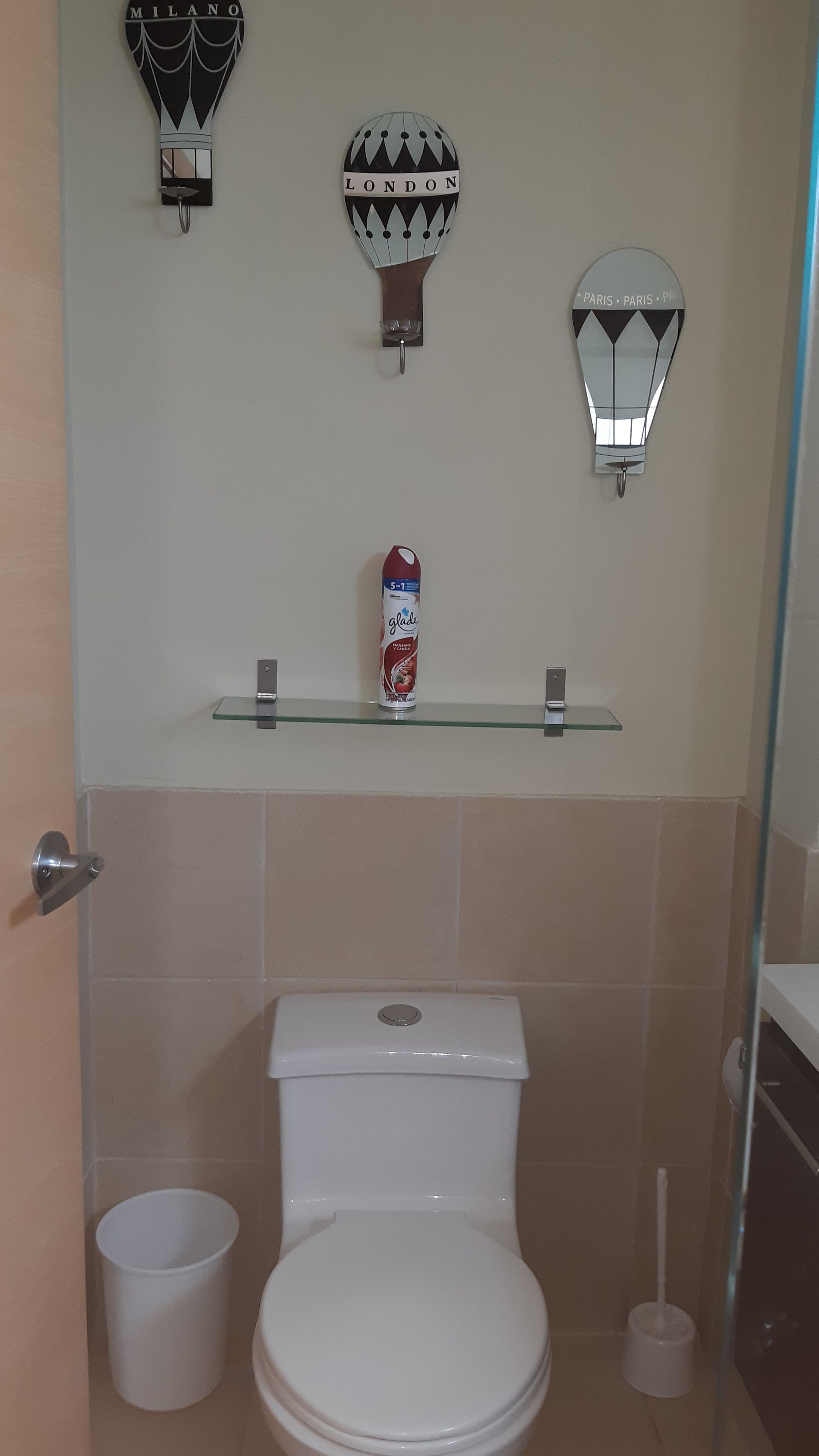 A bathroom with a toilet, a glass shelf with a can of Glace, and decorative wall sconces labeled 'MILANO', 'LONDON', and 'PARIS - PARIS - PF'.