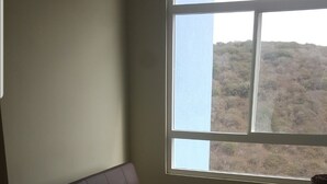 Een kamer met een donkerbruine leren bank, een groot raam met uitzicht op een glooiend landschap en een betegelde vloer.
