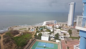 Een kusthotel met uitzicht op het strand, een tennisbaan en een parkeerplaats.
