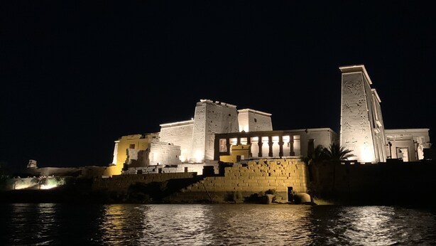 A large, illuminated building with multiple levels and a prominent tower, situated by a body of water. - Villa Misk (Aswan)
