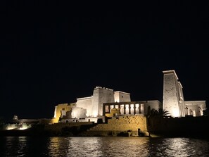 A large, illuminated building with multiple levels and a prominent tower, situated by a body of water. - Villa Misk (Aswan)