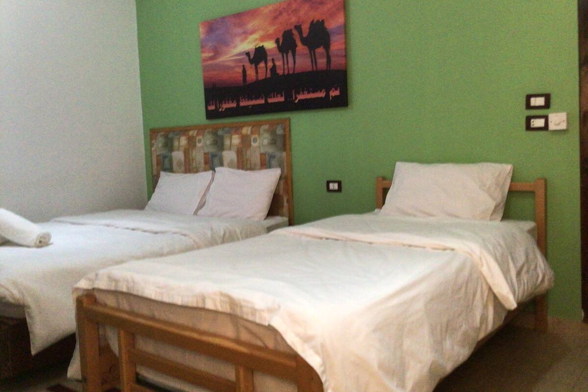 A room with two single beds, a wooden headboard, and a green wall.