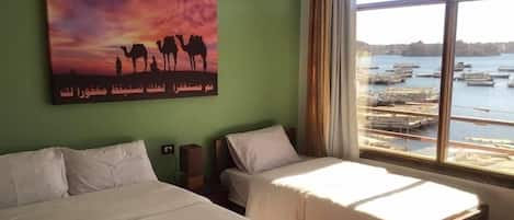 A hotel room with two beds, a large window with a view of boats, and a painting of camels on the wall.