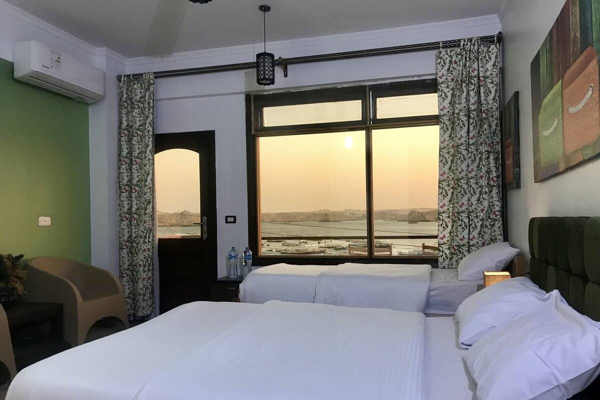A hotel room with two beds, a view of a body of water, and a door leading outside.