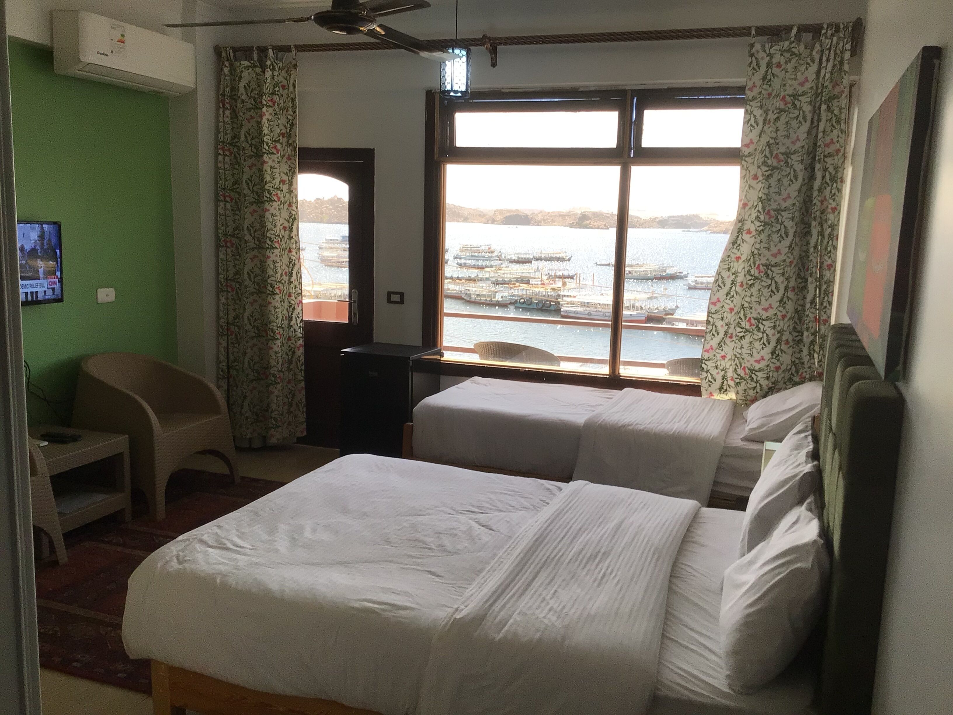 Camera d'albergo con due letti, una scrivania, una sedia e una finestra vista barche e mare.