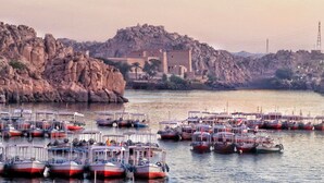 A marina with multiple boats docked, rocky terrain, and a building in the background. - Villa Misk (Aswan)