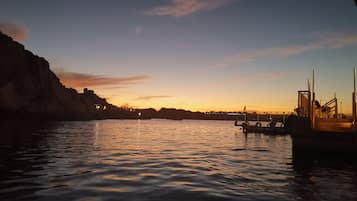 Una orilla tranquila al atardecer con barcos amarrados, un muelle y edificios a la distancia.