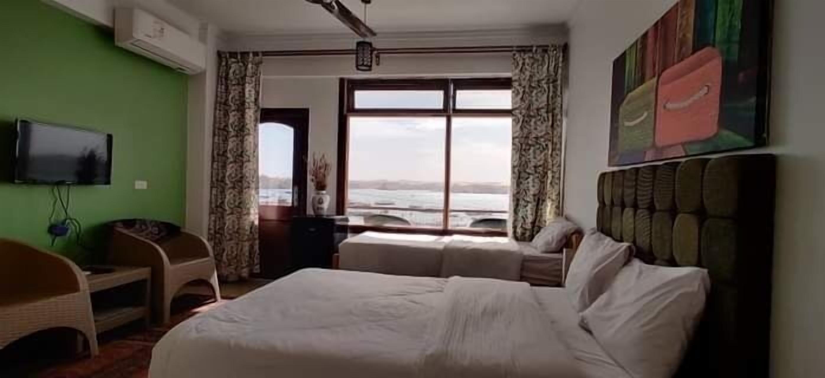 A hotel room with a large bed, a desk, a chair, a television, and a window with a view of the sea.