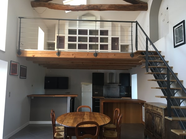 A spacious loft with a high ceiling, a mezzanine level, a kitchen area, and a staircase.
