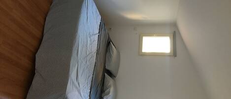 A bedroom with a bed covered in a patterned blanket, two bedside tables, and two wall-mounted windows.