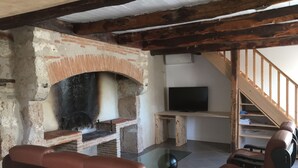 Una sala de estar con chimenea de ladrillo, sofás de cuero, una mesa de centro de vidrio y un televisor sobre un soporte de madera.
