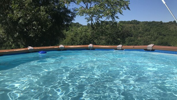 Una piscina azul y transparente con un muelle de madera y vistas a árboles y colinas al fondo.