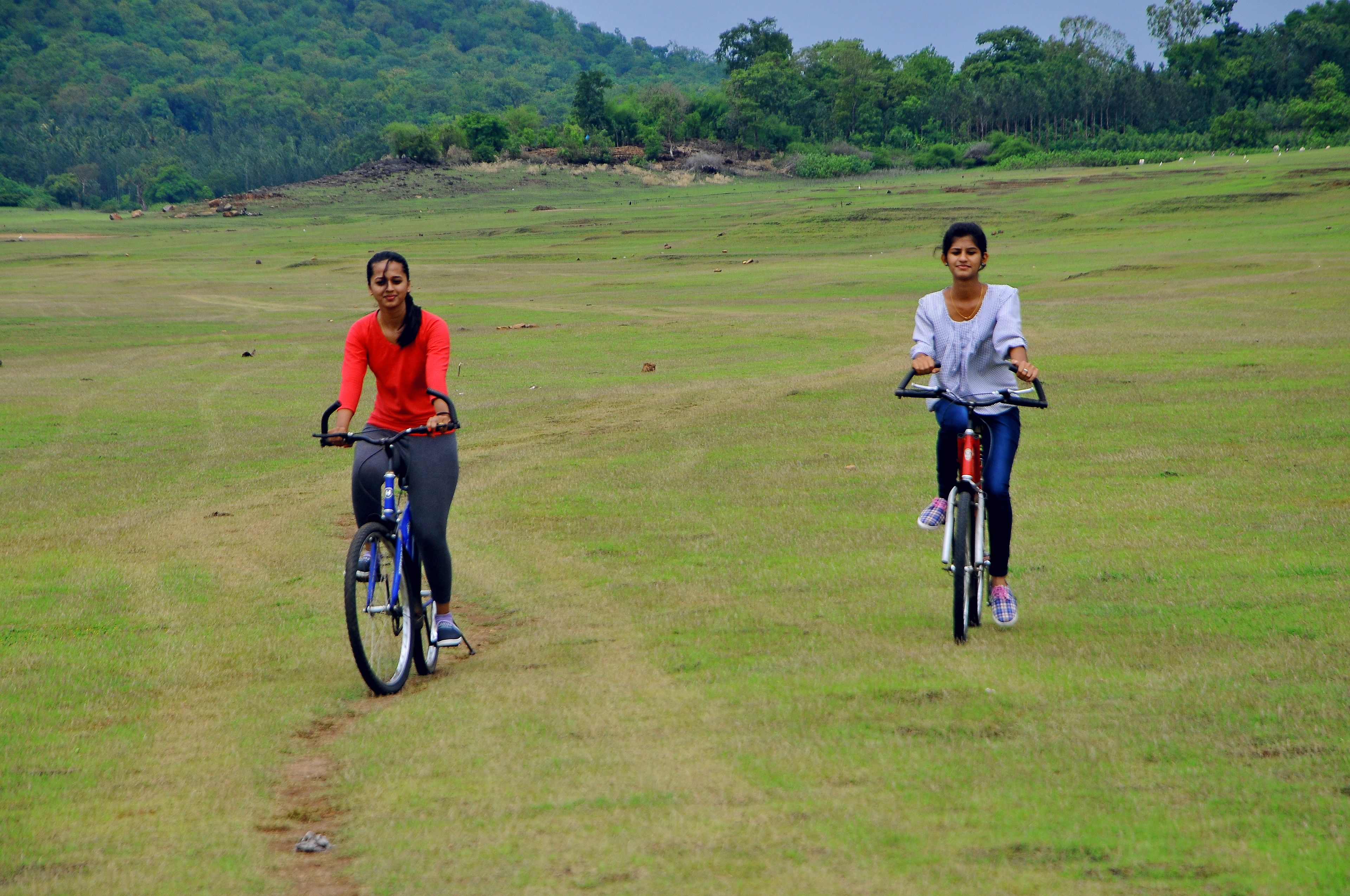 Two people riding bicycles on a grassy field.