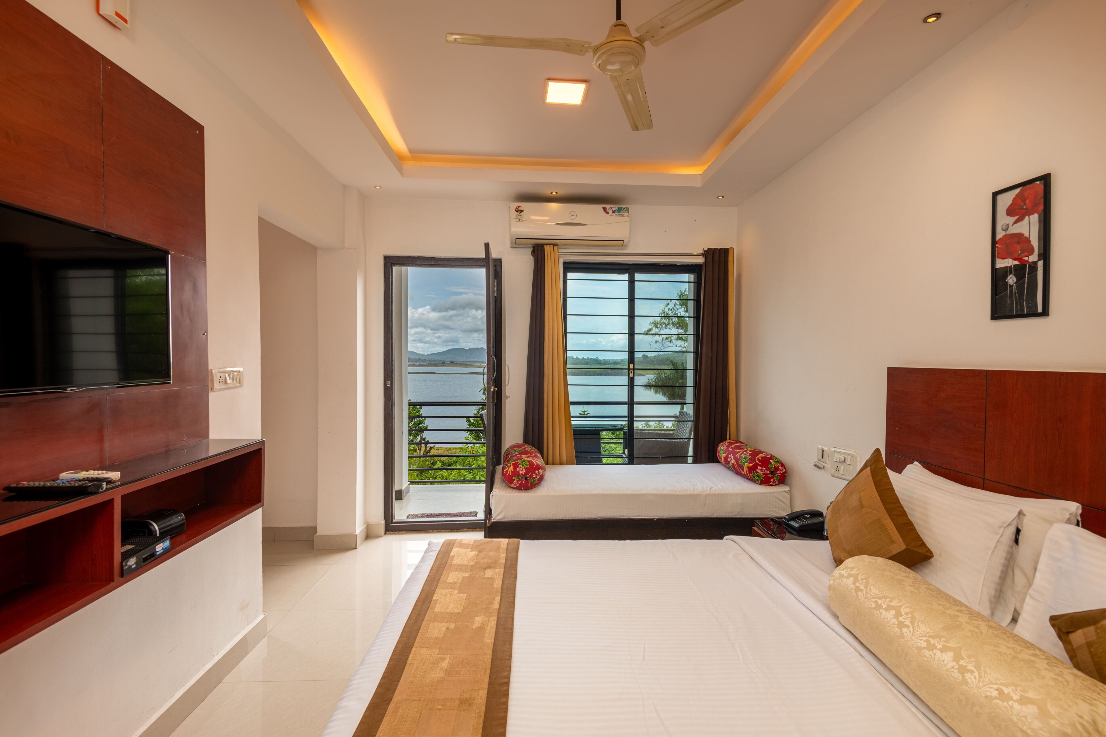A bedroom with a bed, a TV, a ceiling fan, and a view of the outdoors.