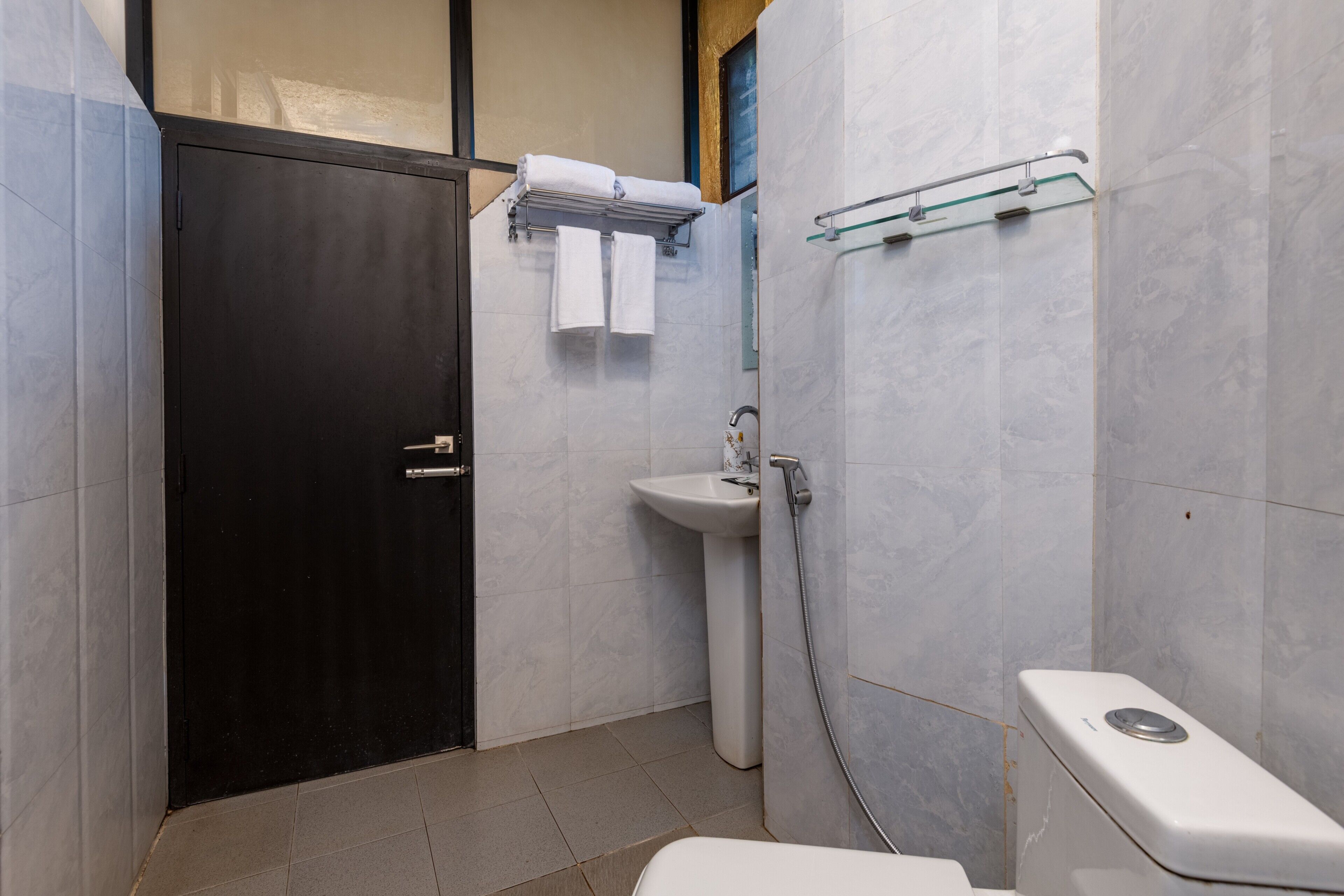 Un baño con puerta negra, lavamanos blanco, cabina de ducha de vidrio y váter blanco.