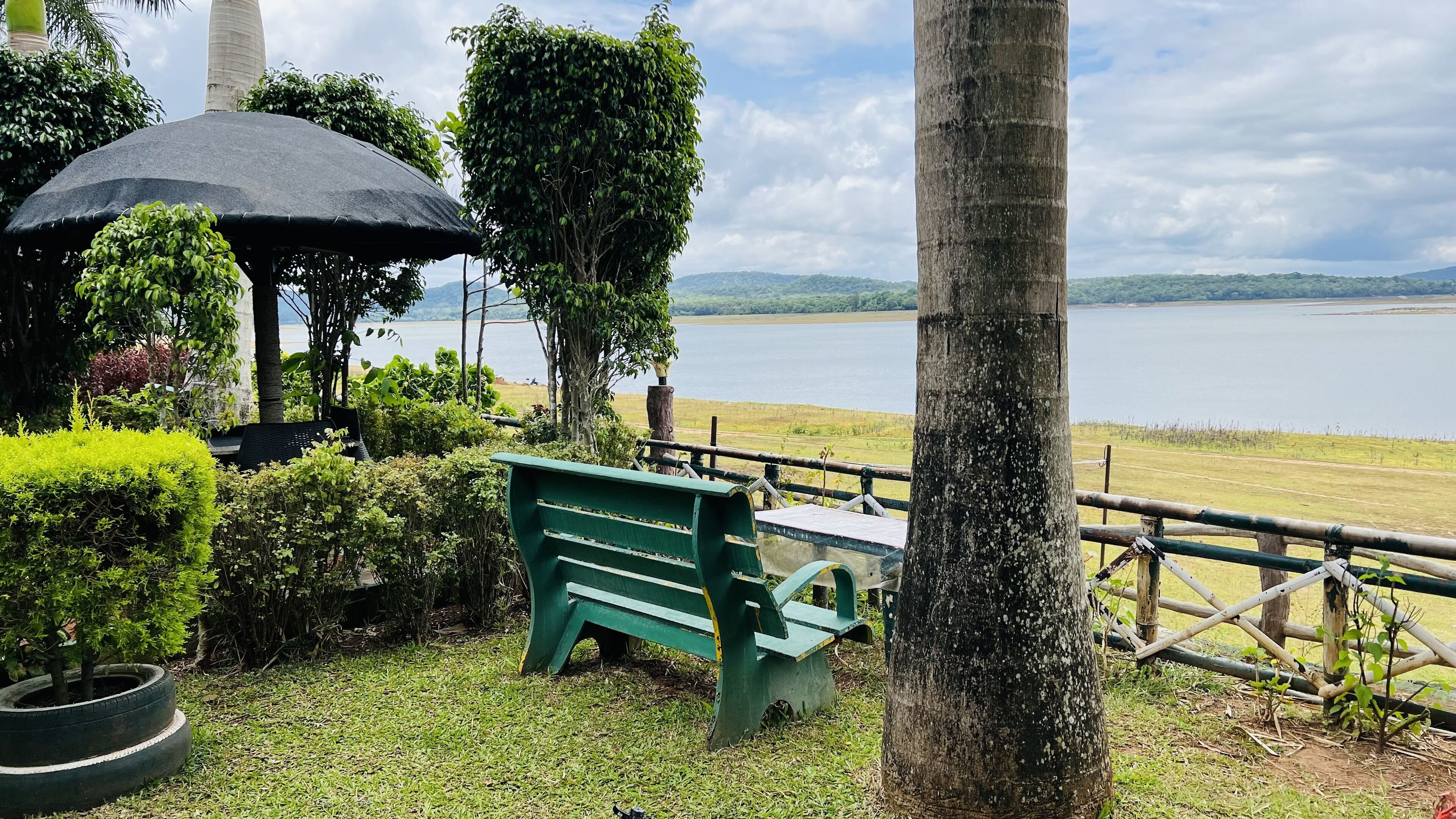 A gazebo with a black canopy, a green bench, and a view of a lake.