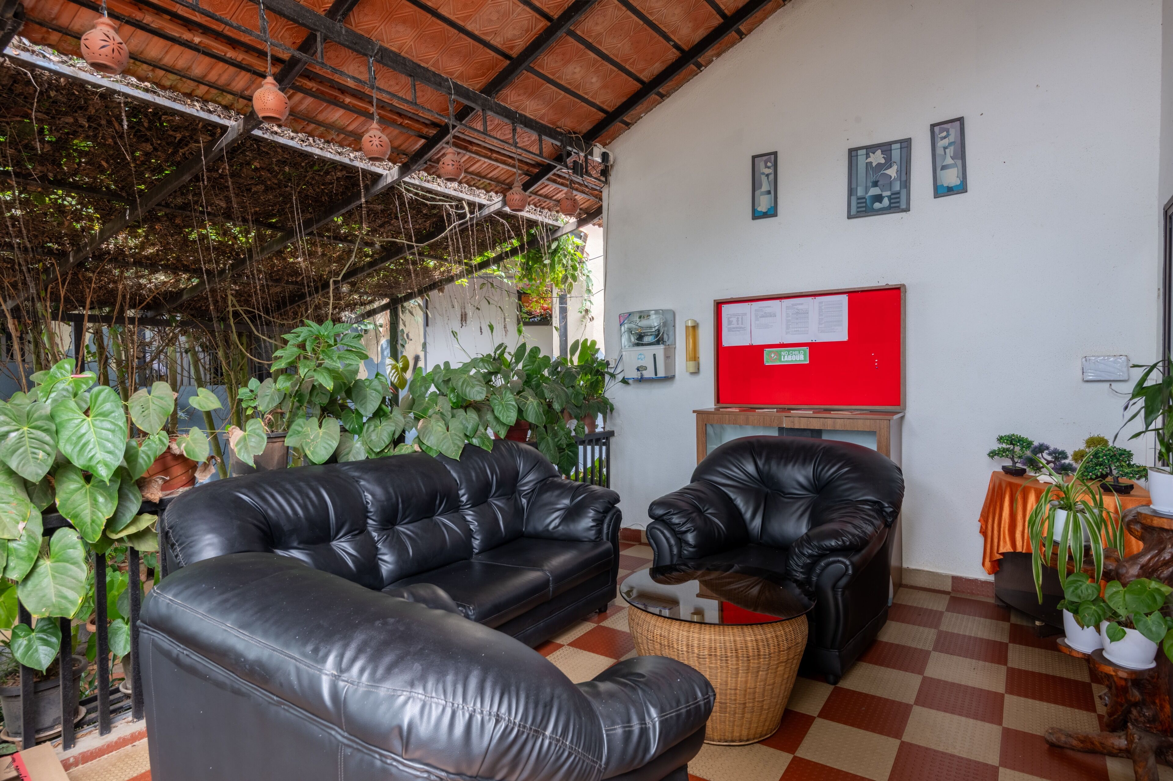 Una habitación con suelo a cuadros, sofás de cuero negro, un tablón de anuncios rojo y varias plantas en macetas.