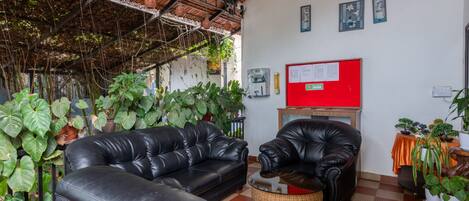 Una habitación con suelo a cuadros, sofás de cuero negro, un tablón de anuncios rojo y varias plantas en macetas.