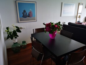 Un coin repas avec une table, des chaises et un vase de fleurs. Il y a un tableau au mur et un miroir au-dessus de la table.