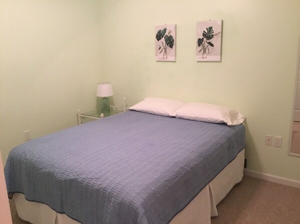 A bedroom with a bed, a bedside table, a lamp, and two wall-mounted plant illustrations.