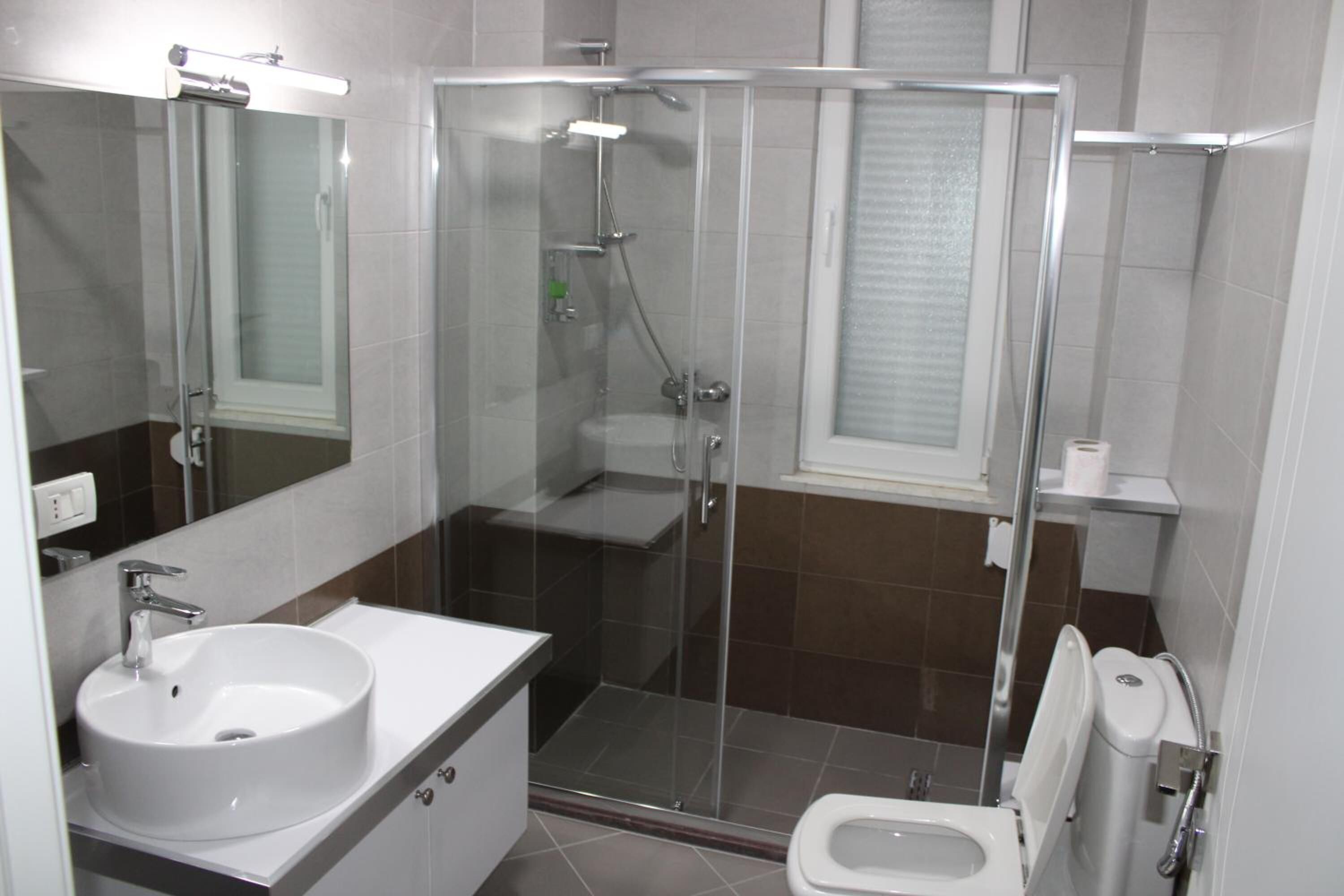 Un baño moderno con ducha envuelta en cristal, lavabo blanco y retrete.