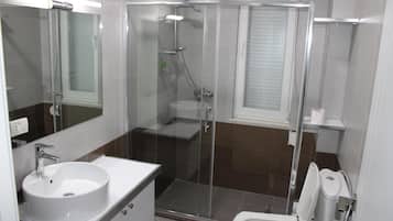Un baño moderno con ducha envuelta en cristal, lavabo blanco y retrete.