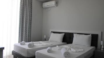 A hotel room with two beds, each with white linens and towels, a bedside table, a lamp, and an air conditioning unit on the wall.